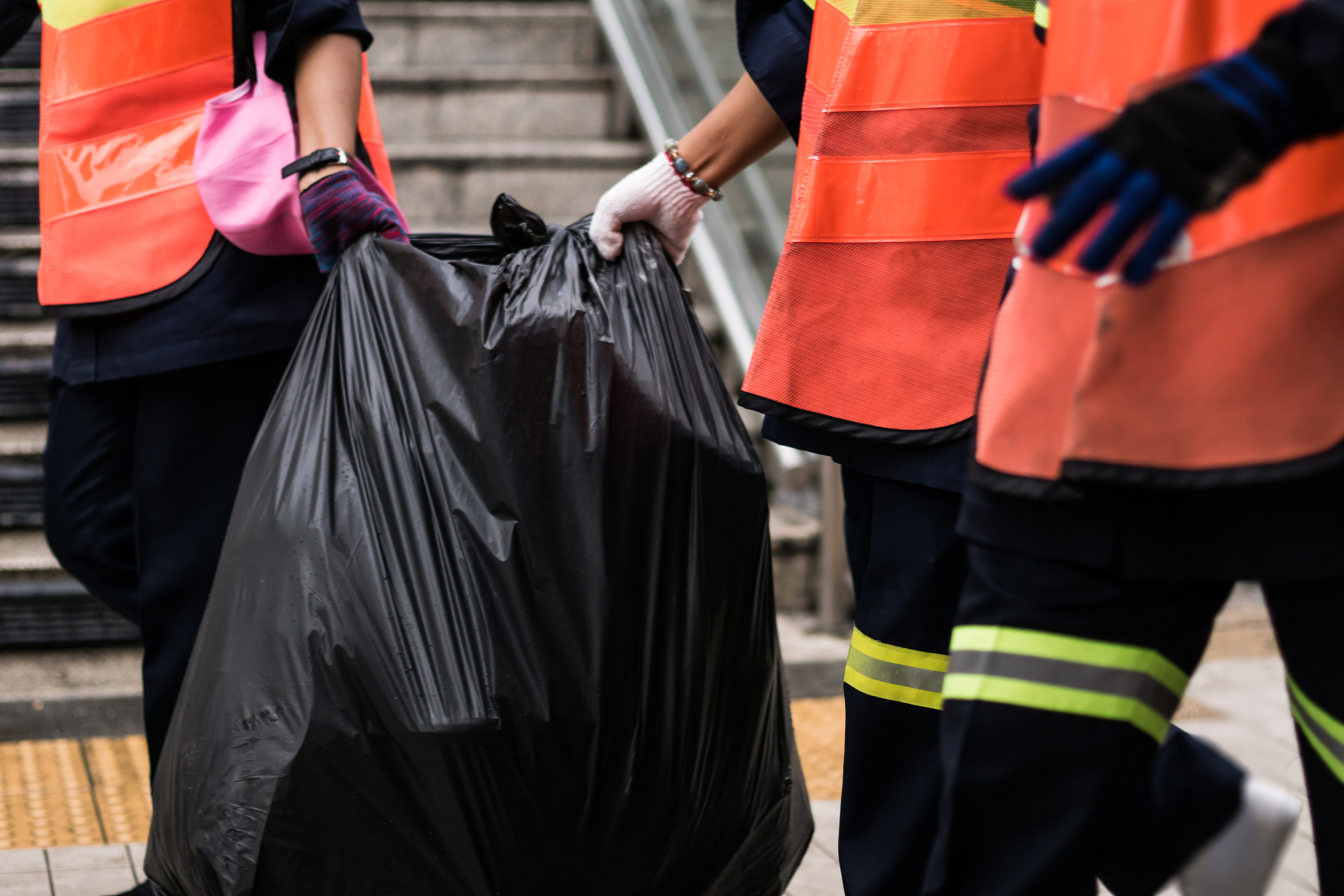 Imagem: profissionais da limpeza carregando sacola com lixo